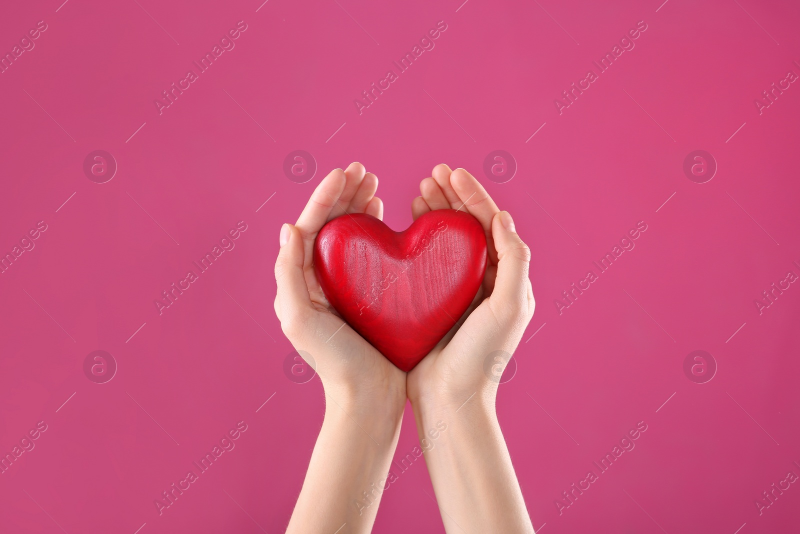 Photo of Woman holding decorative heart in hands on color background, closeup