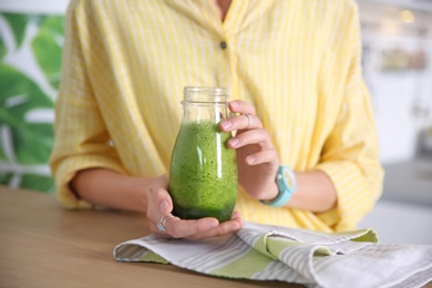 Young woman with bottle of healthy smoothie at table, closeup