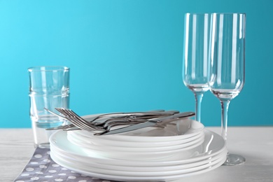 Photo of Set of clean dishes, glasses and cutlery on table against color background