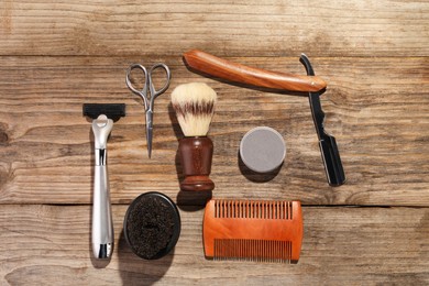 Photo of Moustache and beard styling tools on wooden table, flat lay