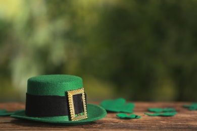 Leprechaun hat and clover leaves on wooden table against blurred background, space for text. St Patrick's Day celebration