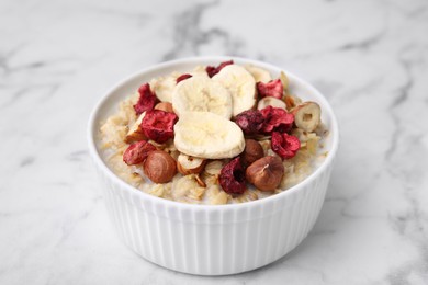 Photo of Delicious oatmeal with freeze dried berries, banana and hazelnuts on white marble table, closeup