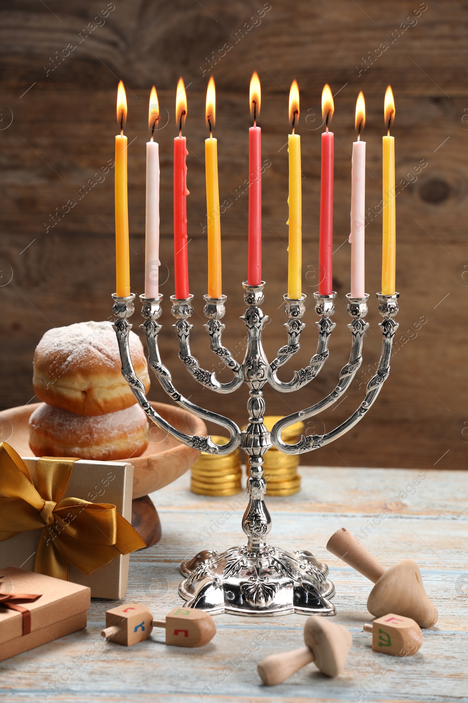 Photo of Hanukkah celebration. Menorah with burning candles, dreidels, donuts and gift boxes on wooden table