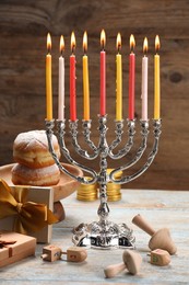 Photo of Hanukkah celebration. Menorah with burning candles, dreidels, donuts and gift boxes on wooden table