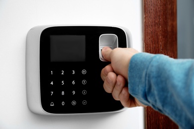 Man scanning fingerprint on alarm system indoors, closeup