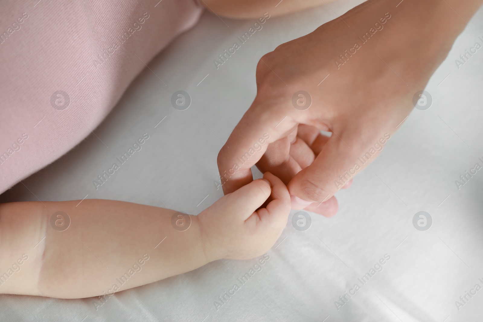 Photo of Baby holding motherʼs hand on bed, closeup