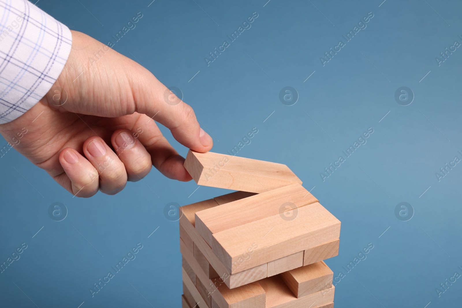 Photo of Playing Jenga. Man building tower with wooden blocks on blue background, closeup