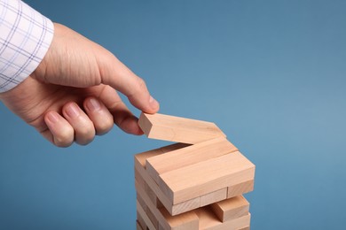 Photo of Playing Jenga. Man building tower with wooden blocks on blue background, closeup