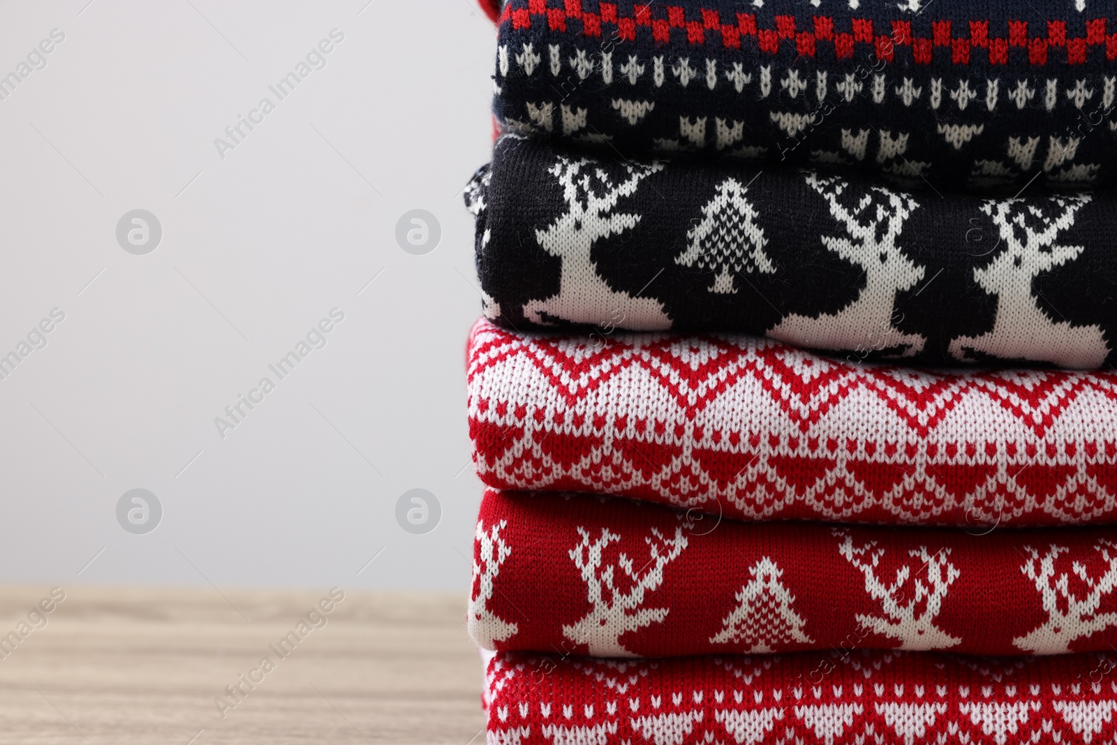 Photo of Stack of different Christmas sweaters on wooden table against light background, closeup. Space for text