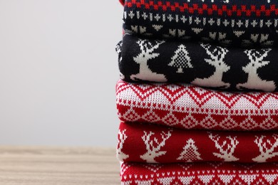 Stack of different Christmas sweaters on wooden table against light background, closeup. Space for text