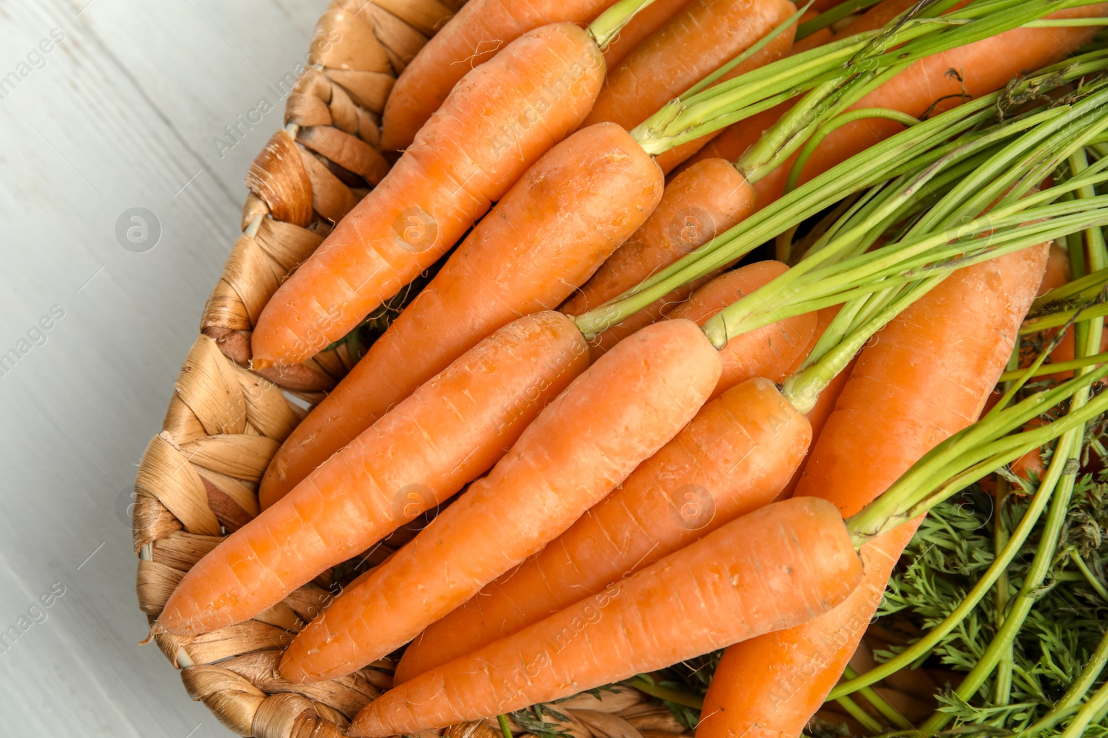 Photo of Wicker tray with ripe carrots on table, closeup