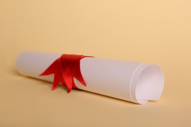 Rolled student's diploma with red ribbon on beige background