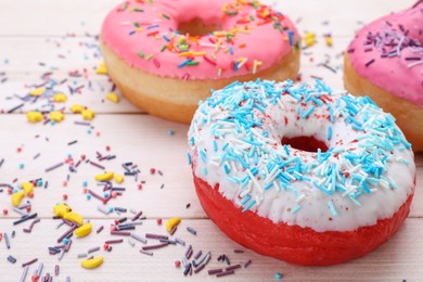 Photo of Glazed donuts decorated with sprinkles on white wooden table, closeup. Space for text. Tasty confectionery