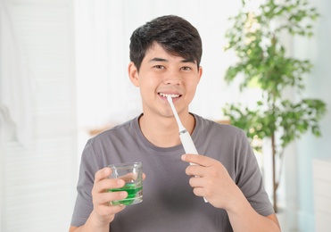 Man brushing teeth and holding glass with mouthwash in bathroom