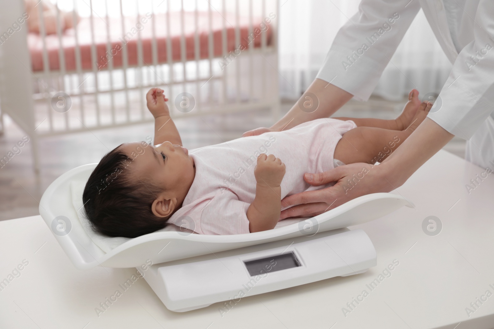 Photo of Doctor weighting African-American baby on scales in light room