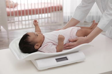 Doctor weighting African-American baby on scales in light room