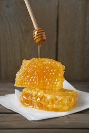 Dripping tasty honey from dipper onto honeycombs on wooden table
