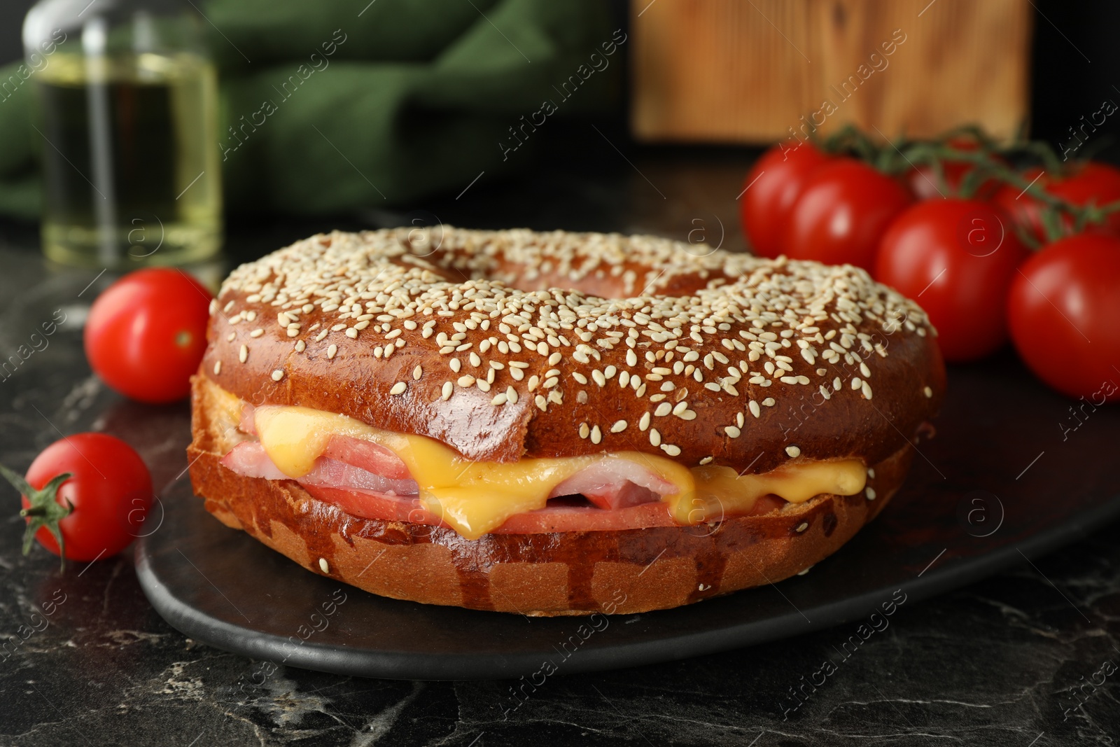 Photo of Delicious bagel with ham and cheese on dark marble table