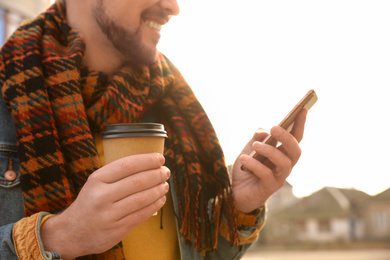 Photo of Man with cup of coffee and smartphone on city street in morning, closeup