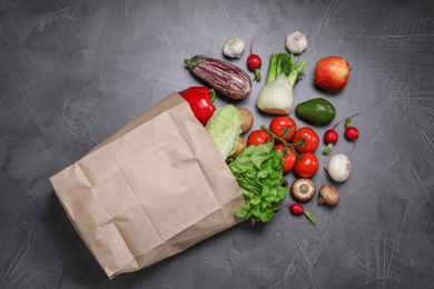 Photo of paper package with fresh vegetables and fruits on dark background, flat lay