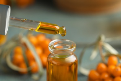 Photo of Natural sea buckthorn oil dripping from pipette into bottle on blurred background, closeup