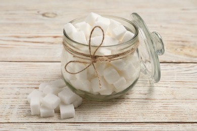 Photo of Glass jar of refined sugar cubes on light wooden table