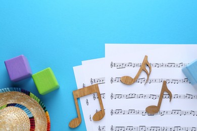 Photo of Baby songs. Music sheets, wooden notes, cubes and hat on light blue background, flat lay