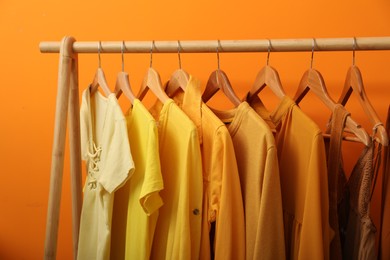 Rack with different stylish women`s clothes near orange wall