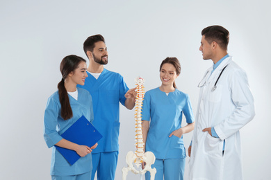 Photo of Professional orthopedist with human spine model teaching medical students against light background