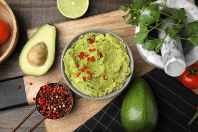 Photo of Bowl of delicious guacamole and ingredients on wooden table, flat lay