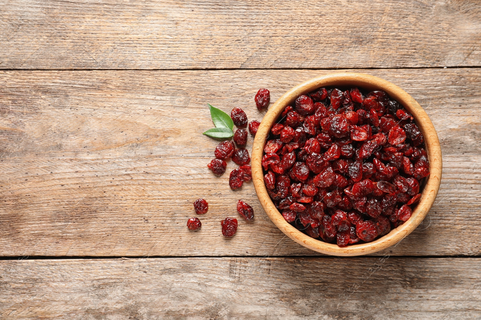 Photo of Bowl with cranberries on wooden background, top view with space for text. Dried fruit as healthy snack