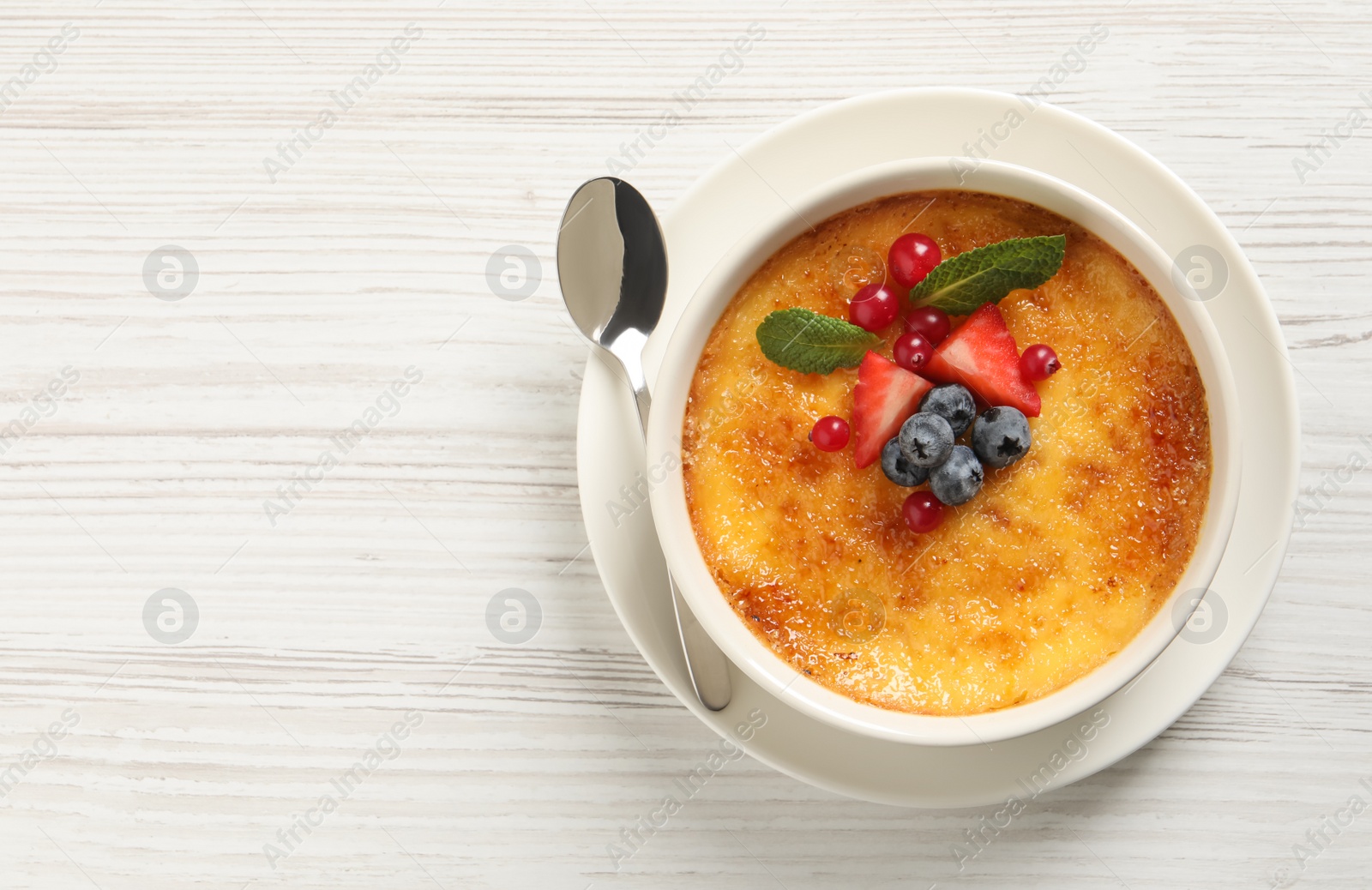Photo of Delicious creme brulee with fresh berries on white wooden table, top view. Space for text