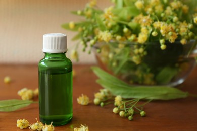 Photo of Bottle of essential oil and linden blossoms on wooden table, closeup. Space for text
