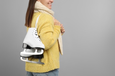 Photo of Happy woman with ice skates on grey background, closeup. Space for text