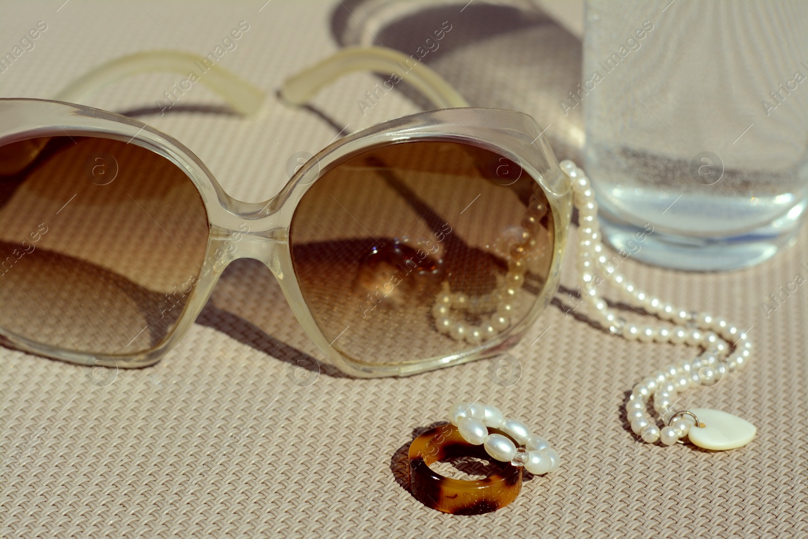 Photo of Stylish sunglasses, glass of water and jewelry on grey surface, closeup