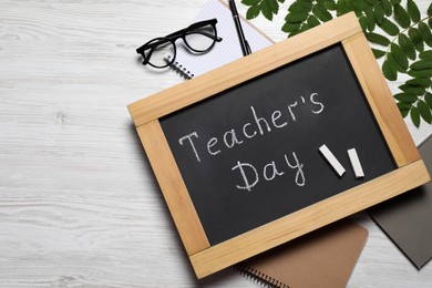 Photo of Blackboard with words Teacher's Day, notebooks and glasses on white wooden table, flat lay