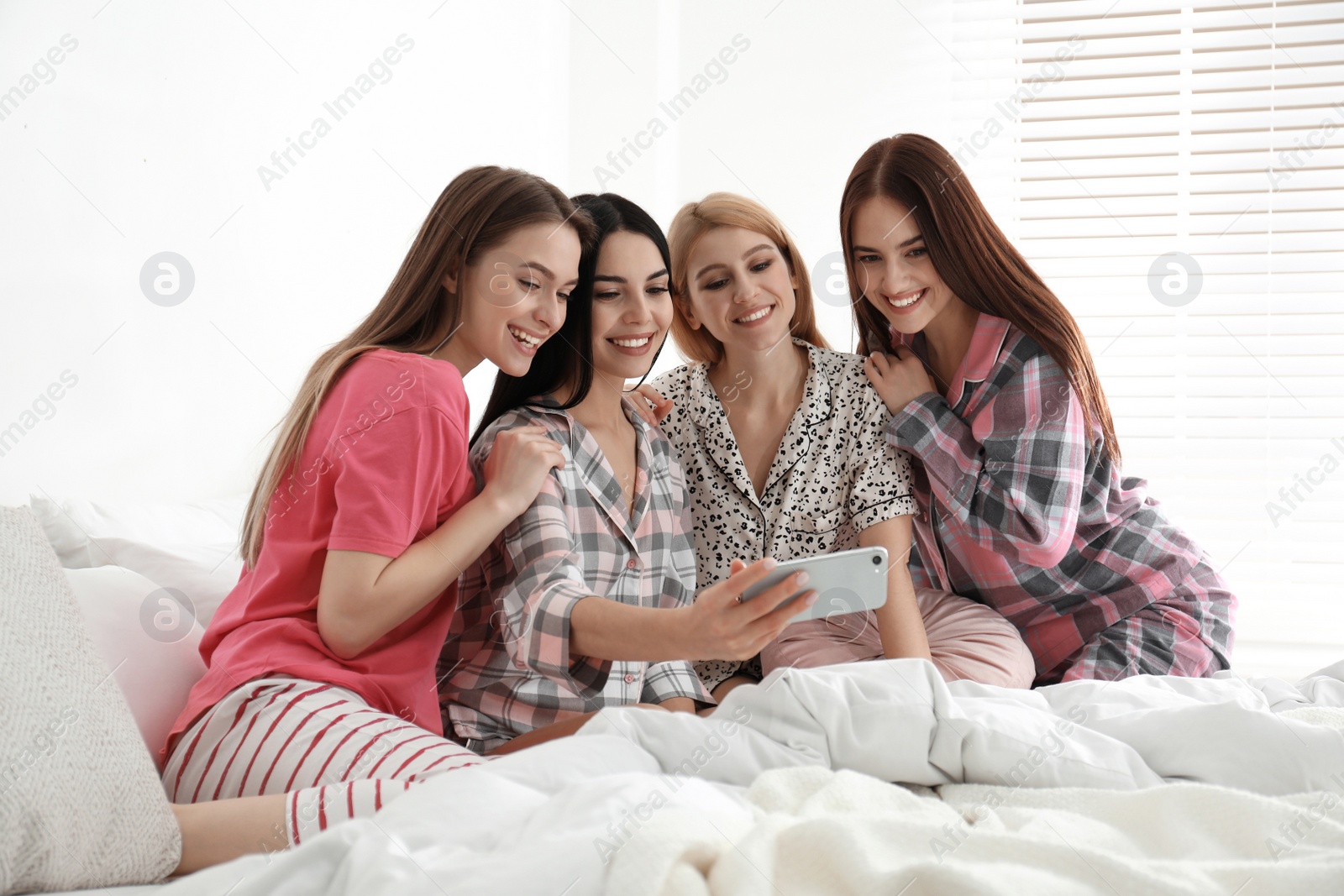 Photo of Beautiful young ladies taking selfie on bed at pamper party. Women's Day