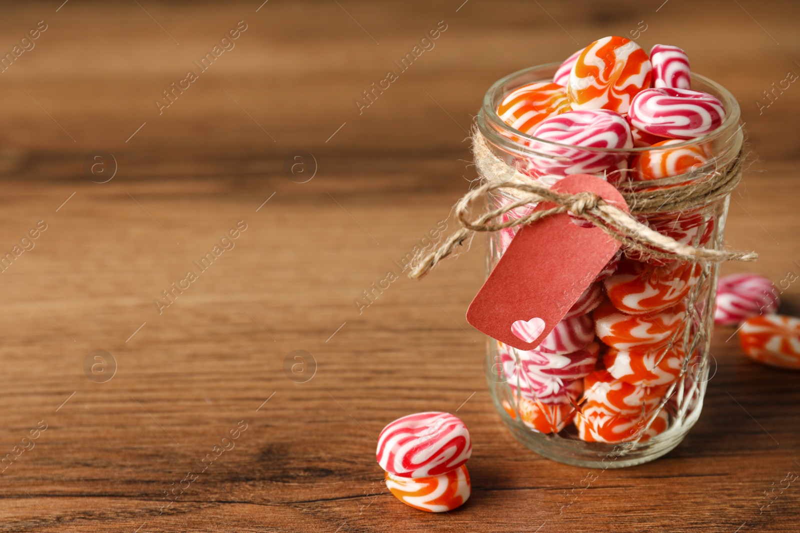 Photo of Color hard candies in glass jar on wooden table. Space for text