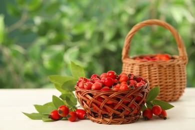 Photo of Ripe rose hip berries with green leaves on white wooden table outdoors