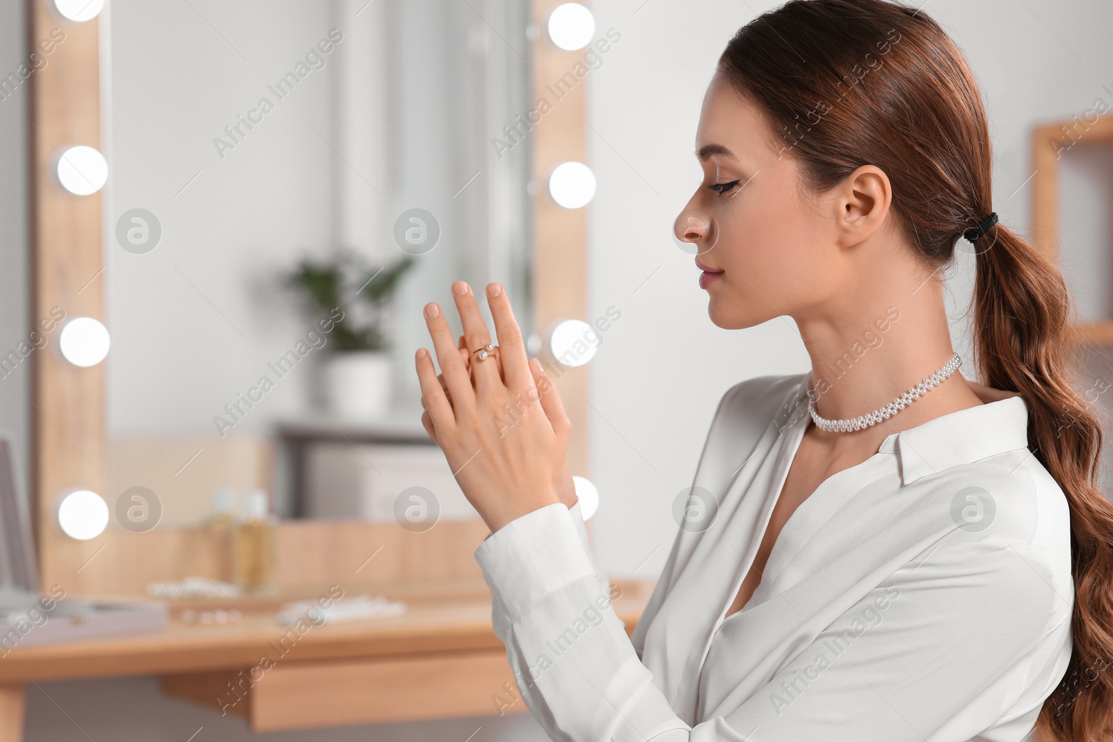 Photo of Young woman trying on elegant ring with pearls indoors, space for text