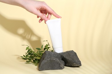 Woman with tube of cream, branches and stones on light yellow background, closeup