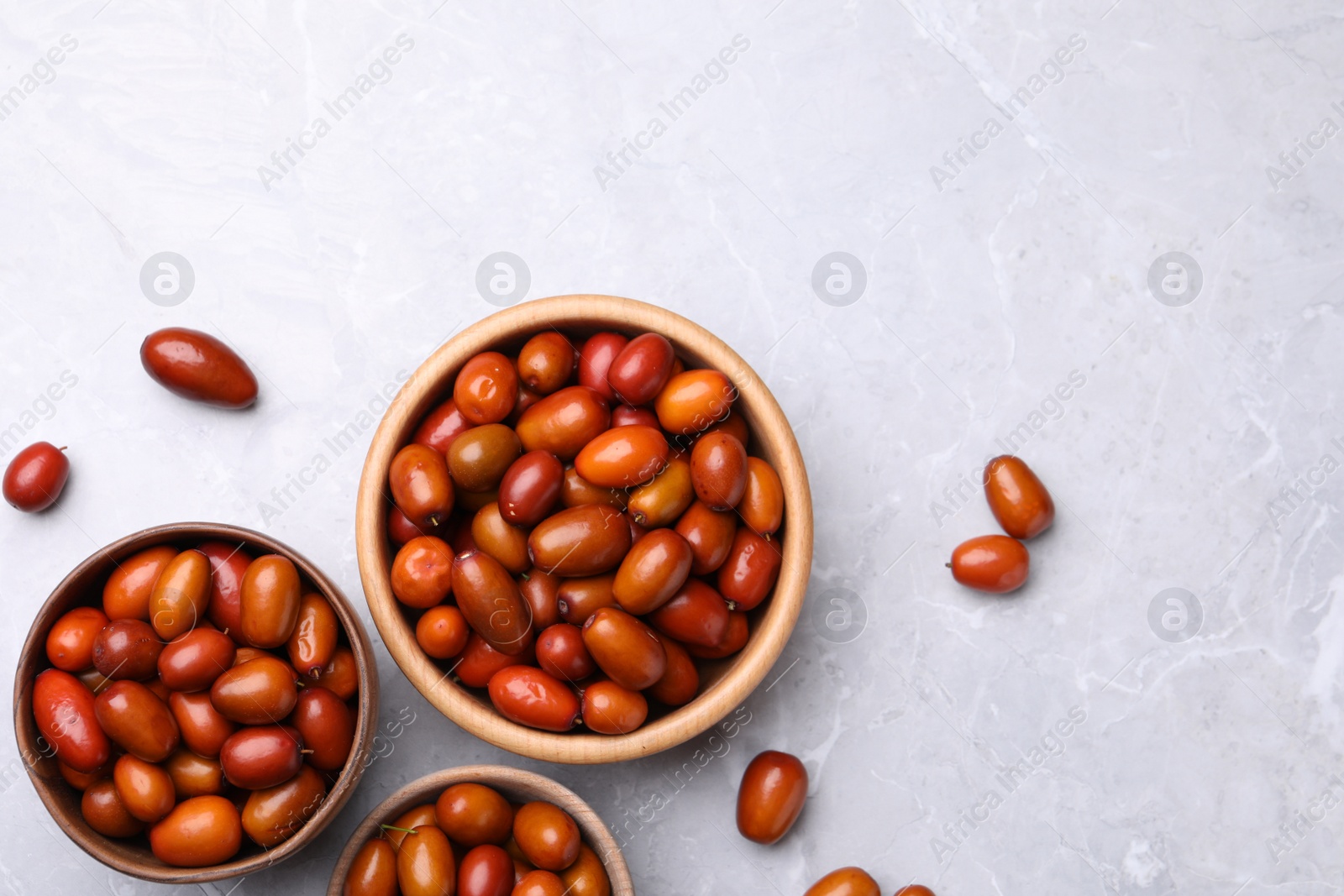 Photo of Fresh Ziziphus jujuba fruits with wooden bowls on light table, flat lay. Space for text