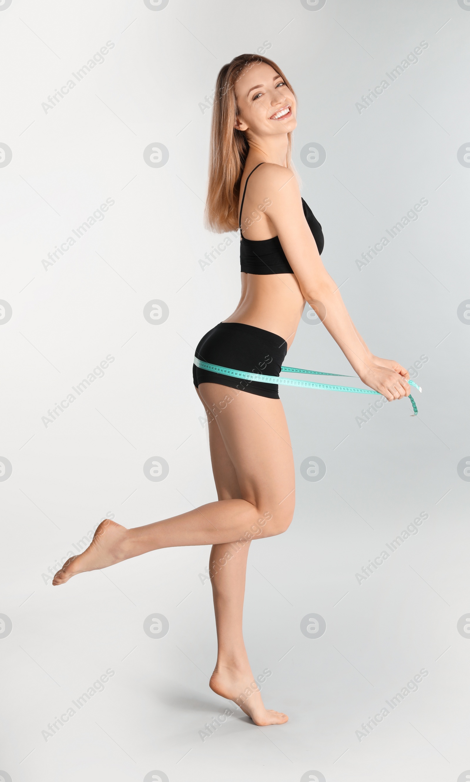 Photo of Slim woman measuring her hips on light background, space for text. Perfect body