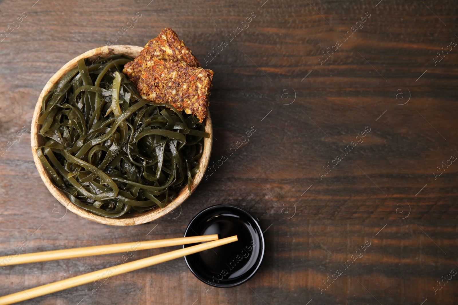 Photo of Tasty seaweed salad in bowl served on wooden table, flat lay. Space for text