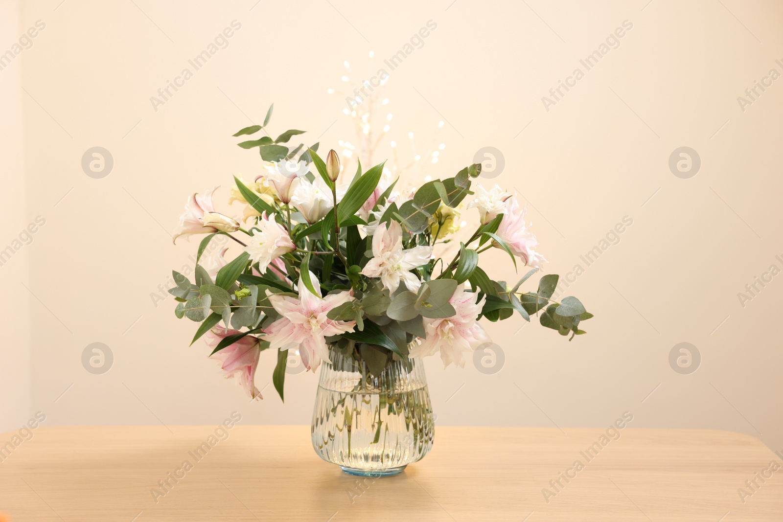 Photo of Bouquet of beautiful lily flowers in vase on wooden table against beige background