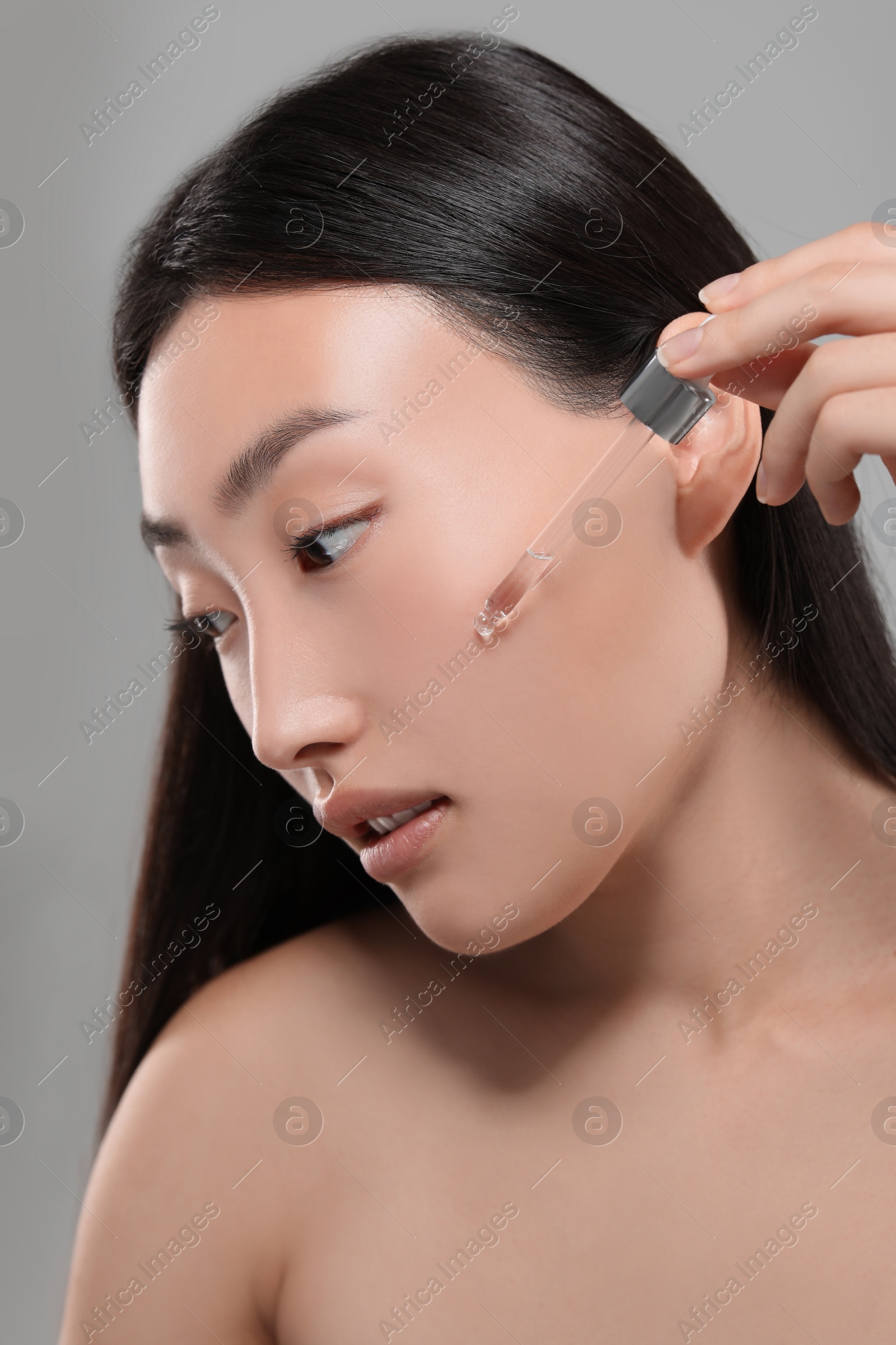 Photo of Beautiful young woman applying cosmetic serum onto her face on grey background