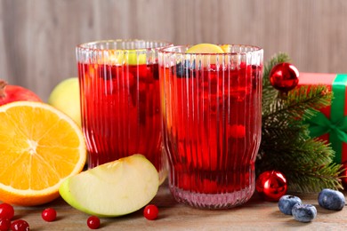Photo of Aromatic Sangria drink in glasses, ingredients and Christmas decor on wooden table