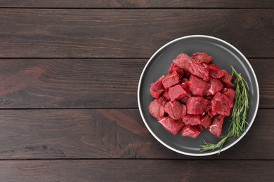 Photo of Pieces of raw beef meat with rosemary on wooden table, top view. Space for text