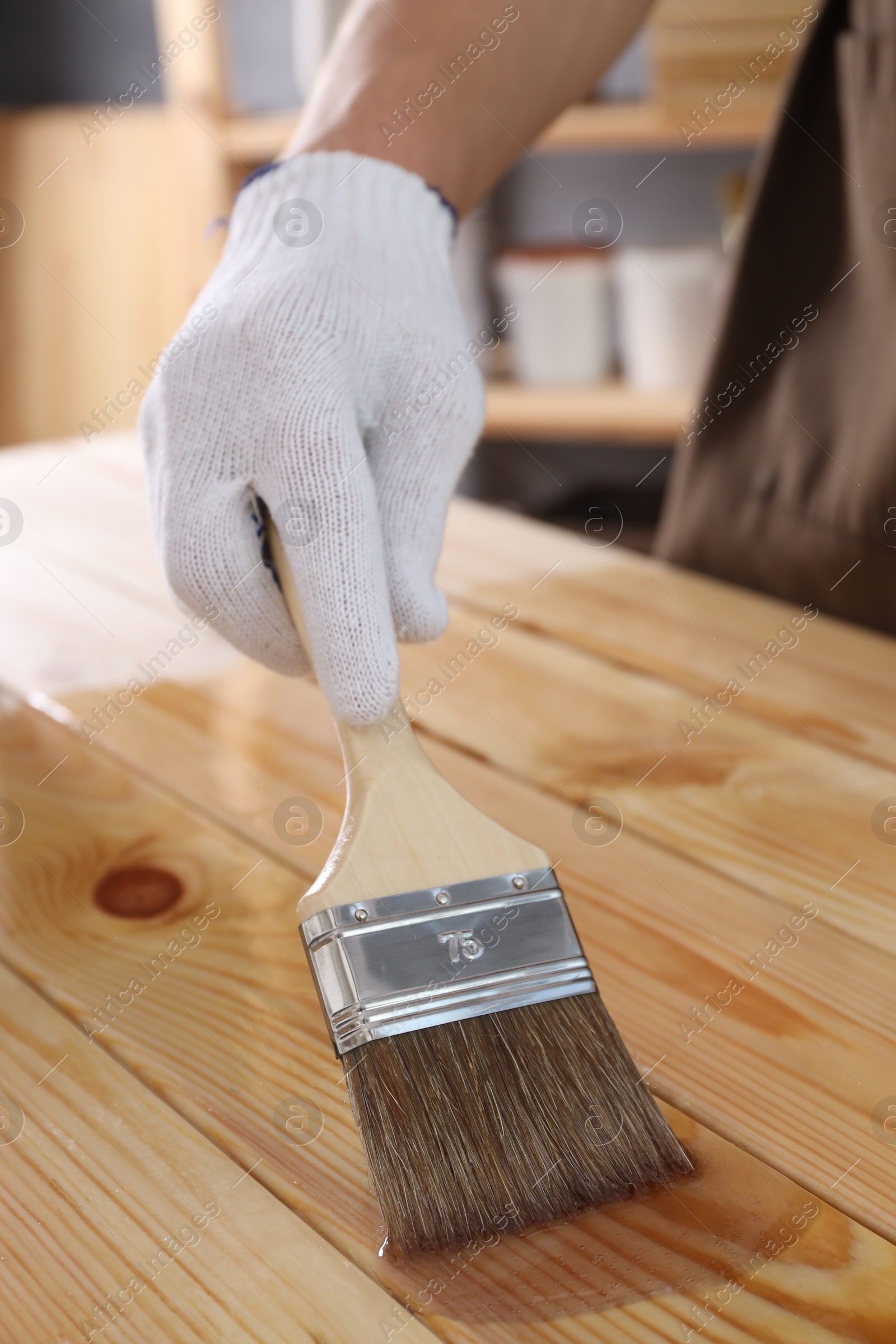 Photo of Man varnishing wooden surface with brush indoors, closeup