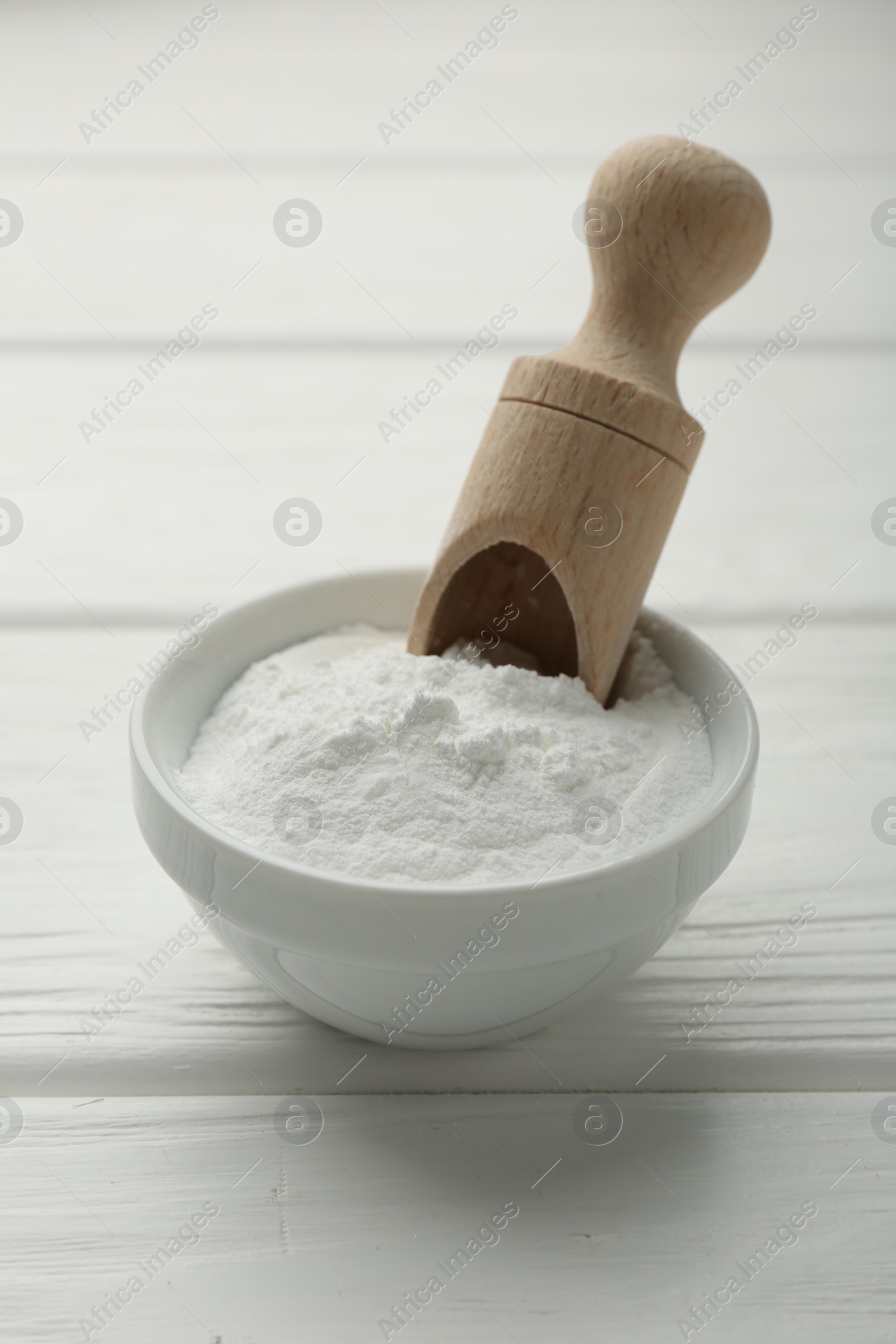 Photo of Baking powder in bowl and scoop on white wooden table